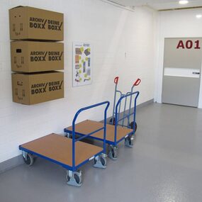 Drei Archivboxen, zwei Transportwagen und ein Lagerraum im Selfstorage-Bereich.